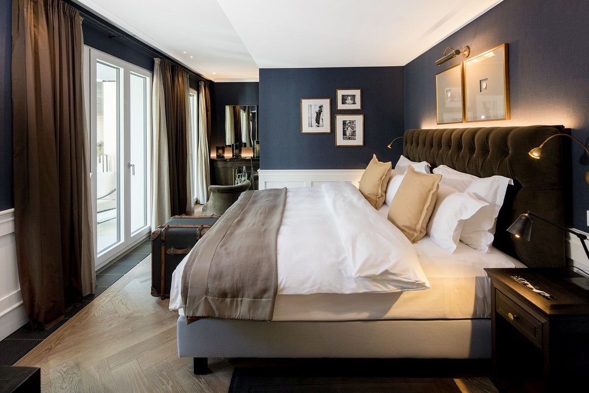 Hotel room with dark blue wallpaper, white painted wall panels, headboard out of dark brown velvet
